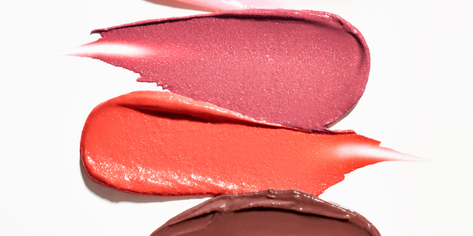 Vier lipstickpatches in verschillende kleuren liggen naast elkaar op een witte oppervlakte.